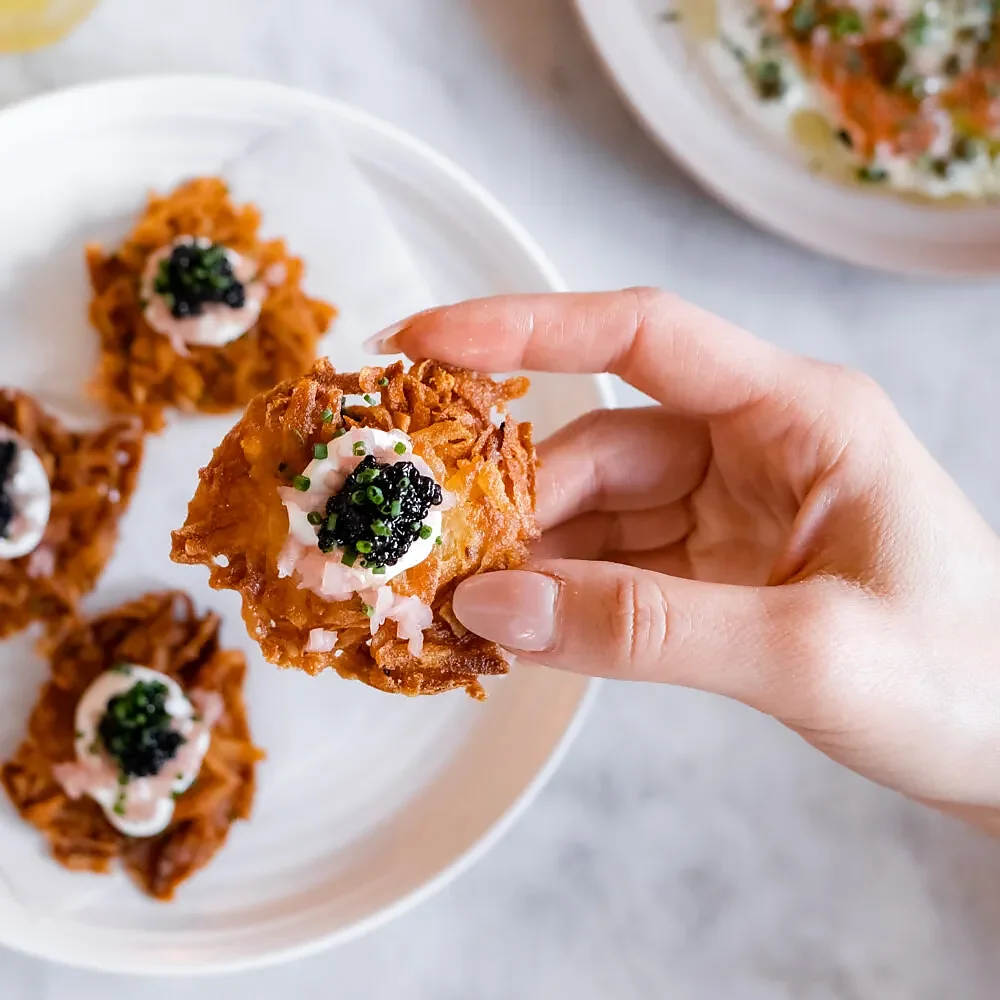 Hand holding potato latke topped with caviar and creme fraiche