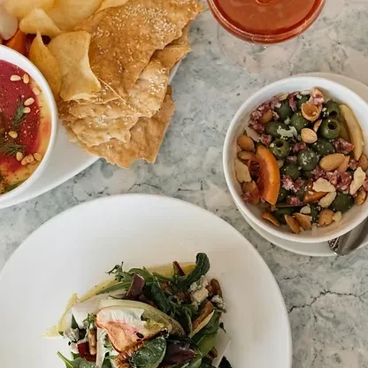 Overhead shot: Table set with dip, flatbread, drink, olives, and a salad.