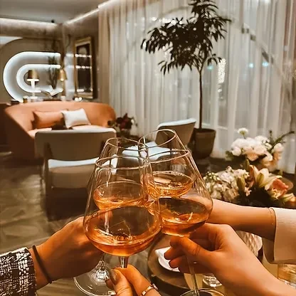 Four hands toast with rosé wine glasses in a warm lounge.