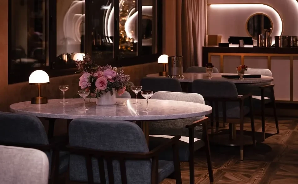 Elegant restaurant: Oval marble table set with roses, champagne, and lamp.