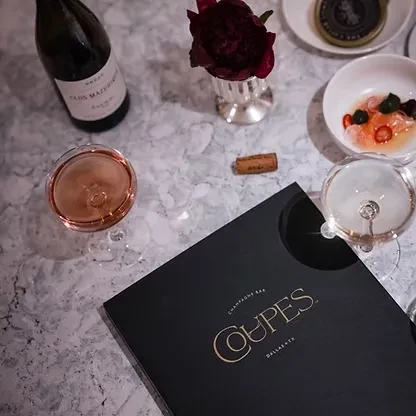 Luxurious table with wine, champagne, small dish, and 'Champagne Bar' menu.