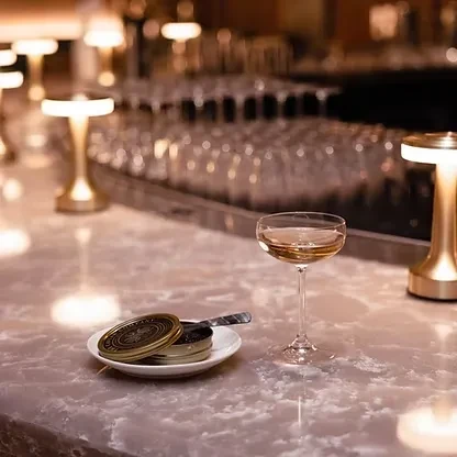 Coupette glass, open caviar tin, on a marble bar counter.