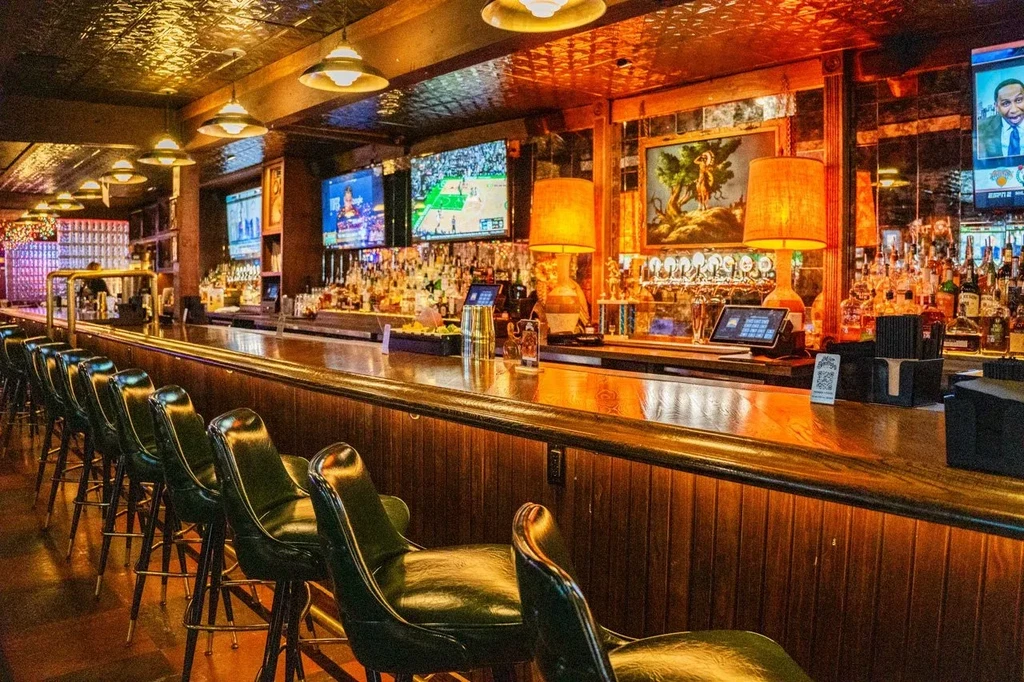 Classic bar interior: long wooden counter, stocked shelves, and sports TVs.