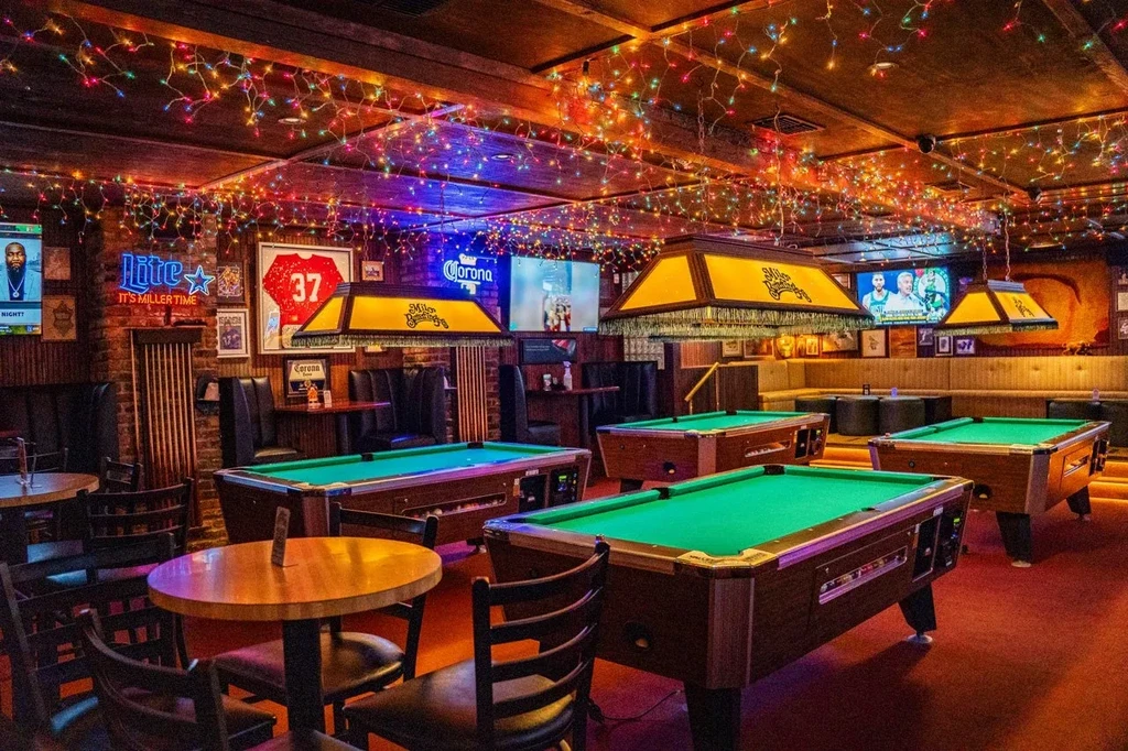 Bar interior with green-felted pool tables, memorabilia, and string lights.