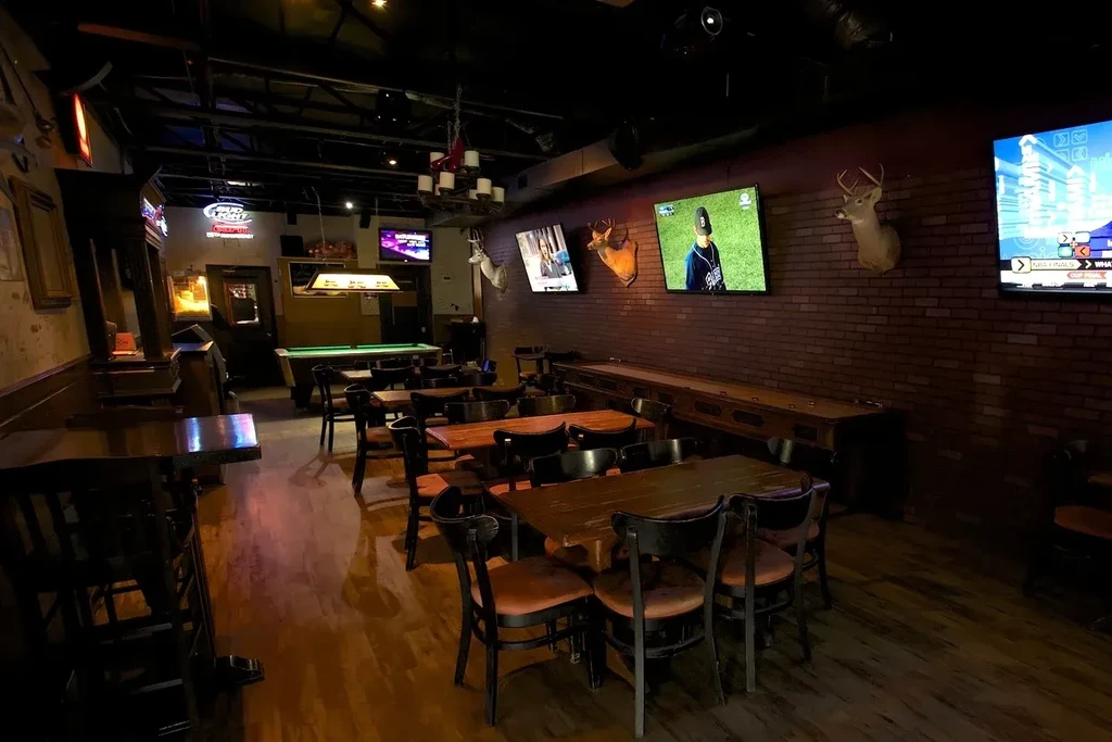 Dimly lit rustic sports bar with tables, bar, TVs, and deer heads.