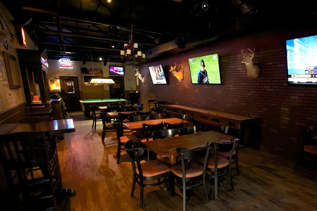 Dimly lit rustic sports bar with TVs, pool table, and shuffleboard.