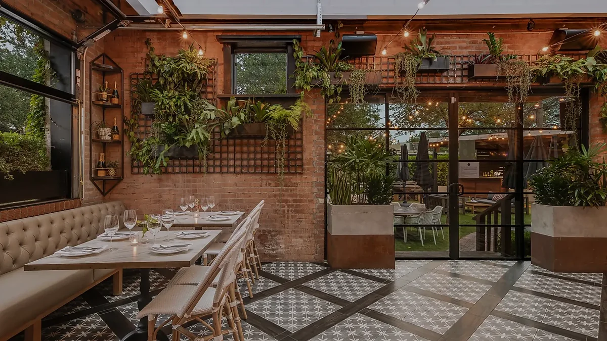 Indoor-outdoor dining room with banquette seating, plants, and string lights