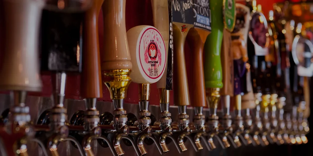 Various beer taps, one with a red owl logo, in a dimly lit bar.