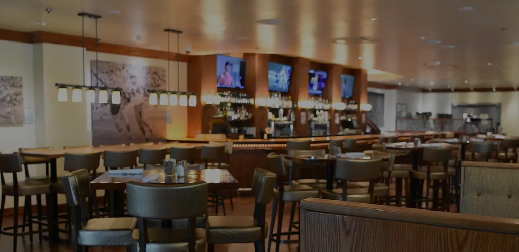 Dimly lit sports bar interior with high-top tables, stocked bar, and TVs.