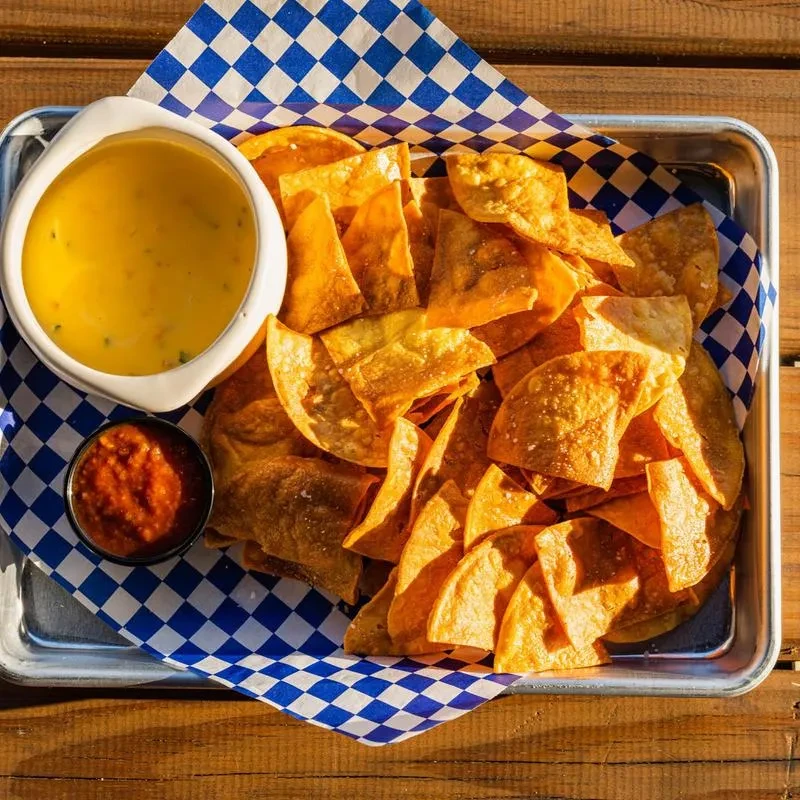 A metal tray of tortilla chips, creamy queso, and chunky salsa.