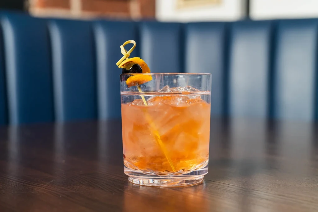 Amber-orange cocktail in a textured lowball glass with orange peel garnish.