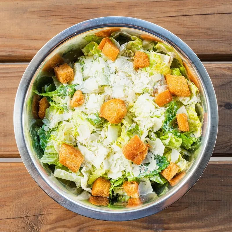Overhead Caesar salad in metallic bowl, romaine, Parmesan, croutons.