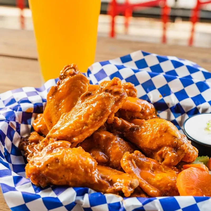 Basket of buffalo chicken wings with dipping sauce, carrots, and celery.