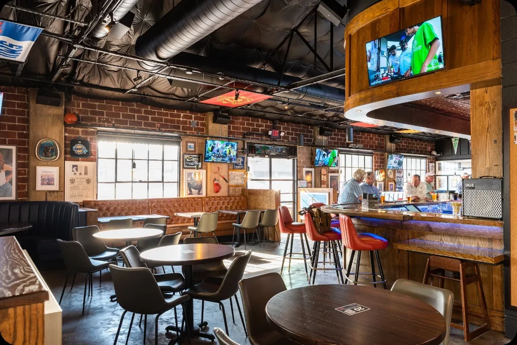 Industrial-rustic sports bar interior with tables, a wooden bar, and people.
