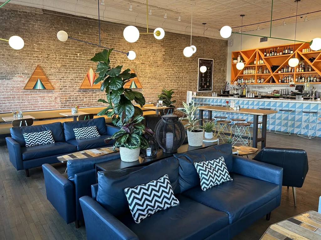 Modern restaurant interior with navy sofas, red brick walls, and vibrant orange bar.