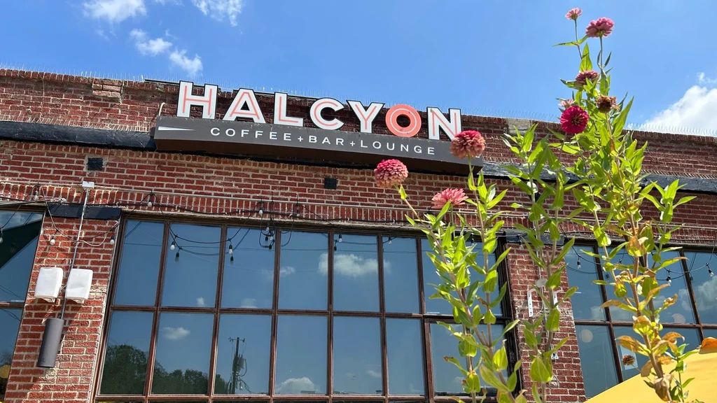 Brick building exterior with "HALCYON COFFEE + BAR + LOUNGE" sign and pink flowers.