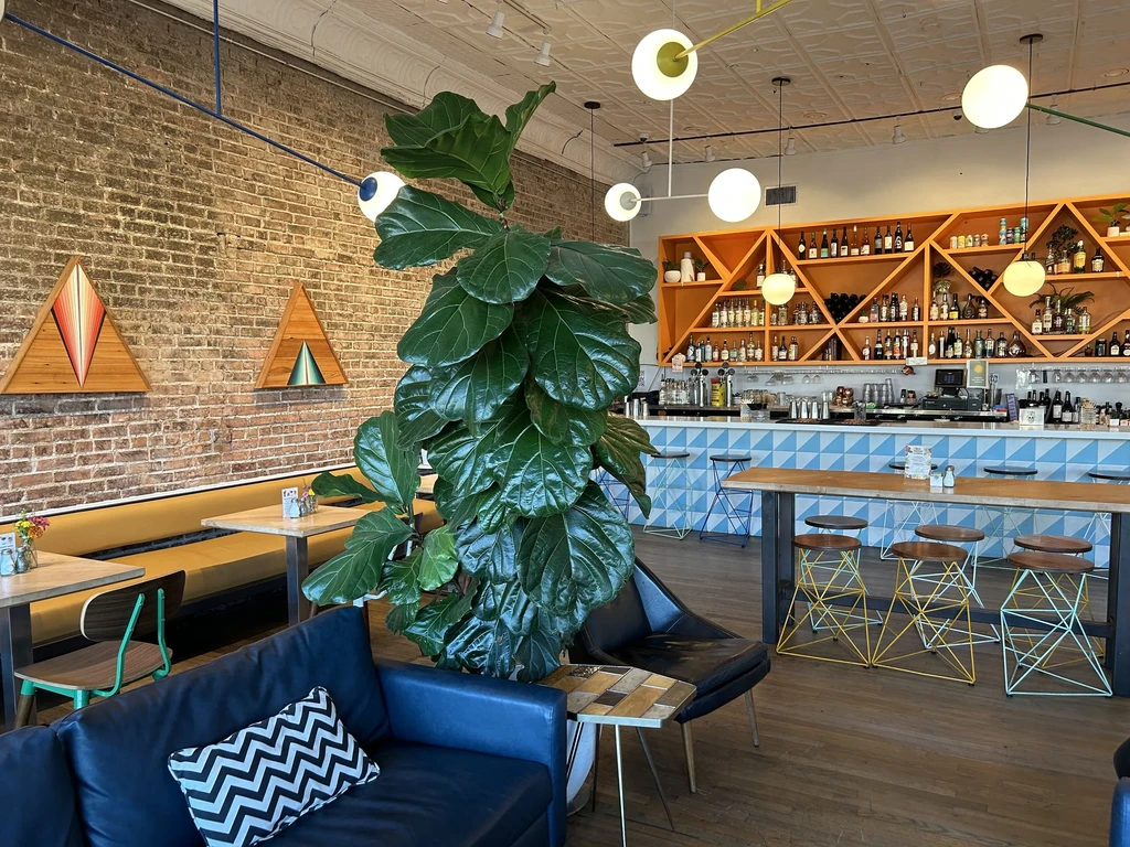 Modern restaurant interior with blue-tiled bar, yellow booth, and fig plant.