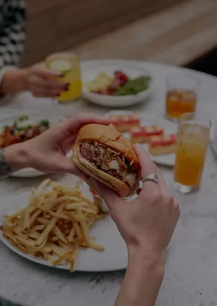 Close-up of hands holding a gourmet burger with fries.