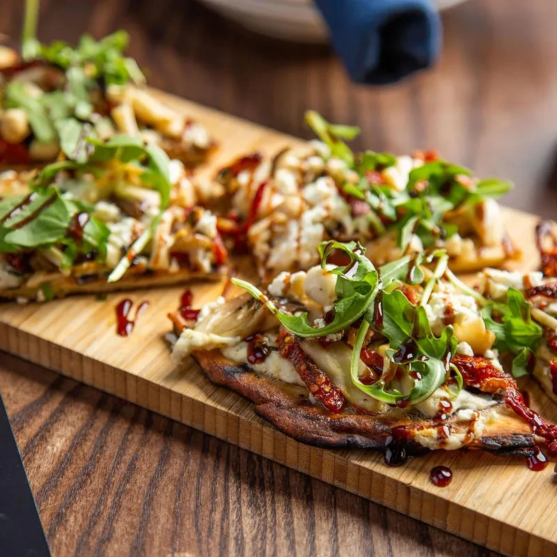 Artisan flatbread slices with arugula, sun-dried tomatoes, cheese, and balsamic glaze.