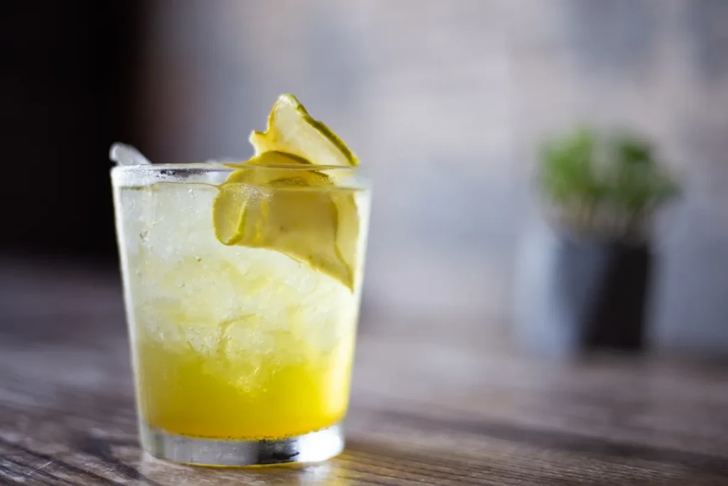 Vibrant yellow drink with crushed ice, lime, and condensation on wood.