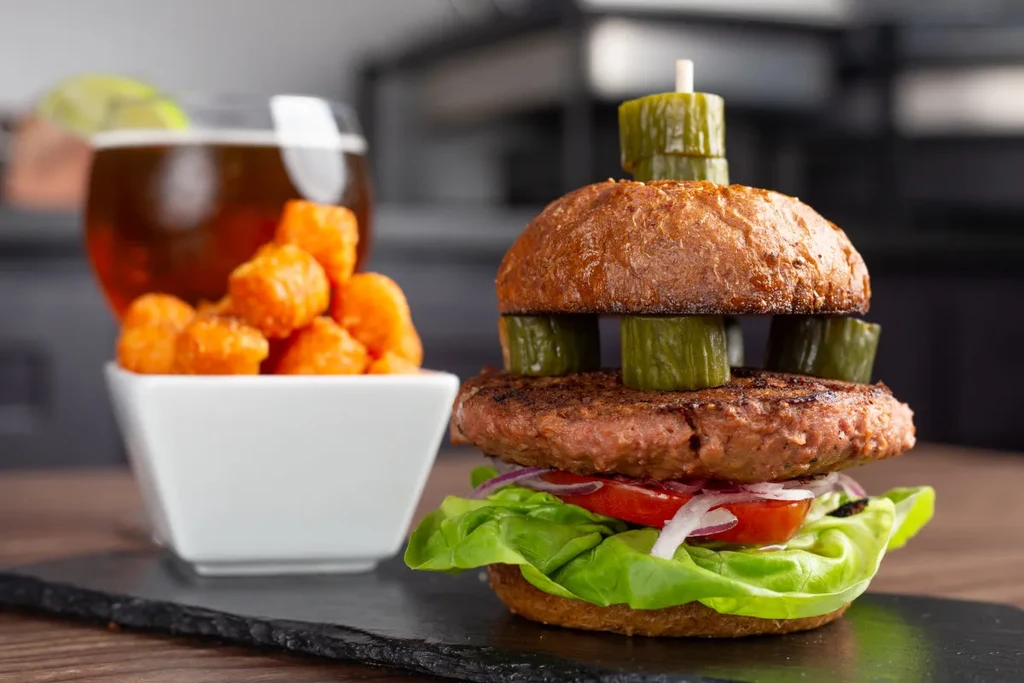 Gourmet open-faced burger, fried tots, and beer on a slate board.