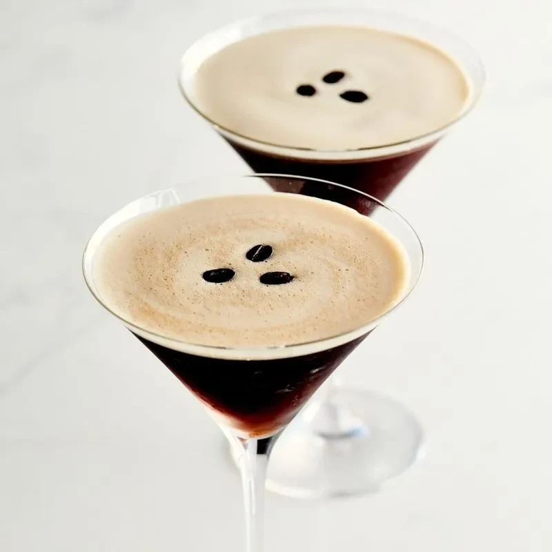 Two martini glasses with coffee drinks, frothy foam, and three beans.