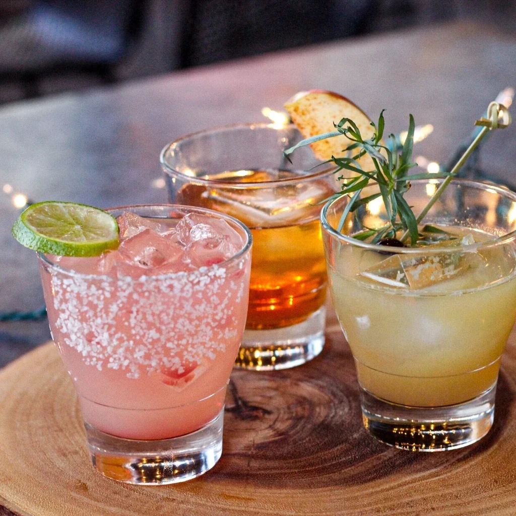 Three colorful, garnished cocktails on a rustic wooden board.