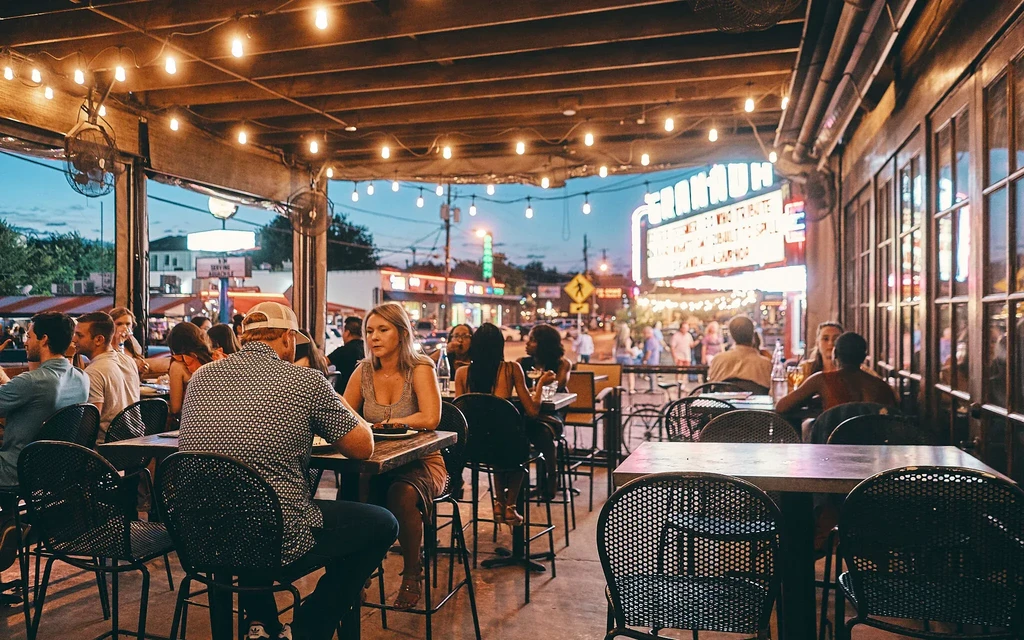 Urban restaurant patio at dusk, busy with diners under string lights.