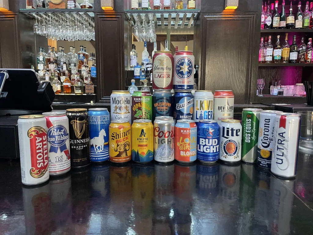 Bar counter filled with diverse beer cans, liquor bottles, and glasses.
