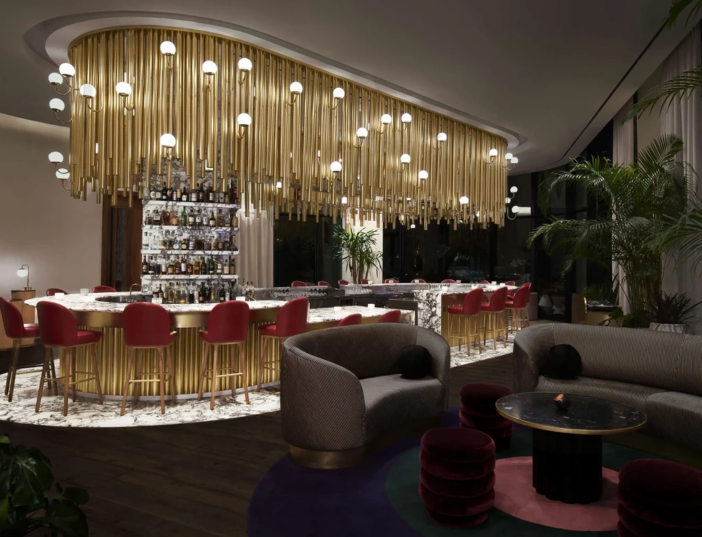 High-end bar and lounge with marble counter, red stools, brass chandelier.