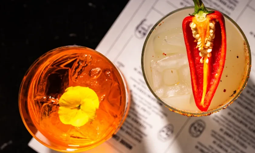 Two cocktails from above; yellow flower garnish, red chili garnish.