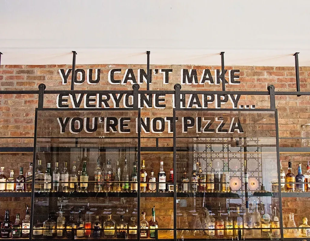 Brick wall bar with humorous pizza quote and tiered liquor bottles.