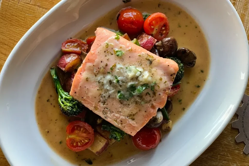 Salmon with herbs, roasted vegetables, and light brown creamy sauce.