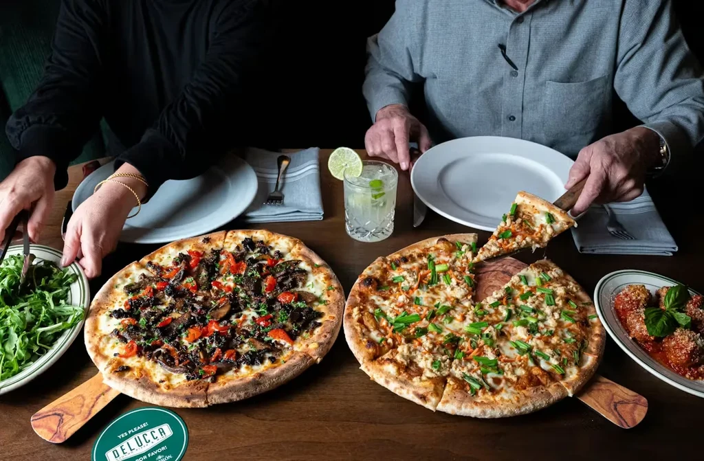 Overhead view of a restaurant table with two pizzas, salad, meatballs, cocktail.