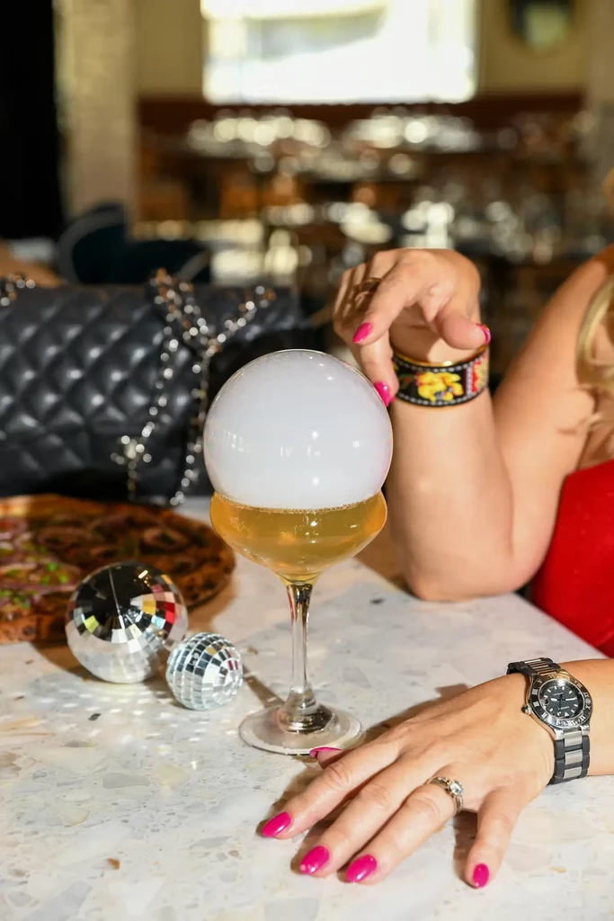Smoked cocktail in coupe glass, person's hands, and disco balls.