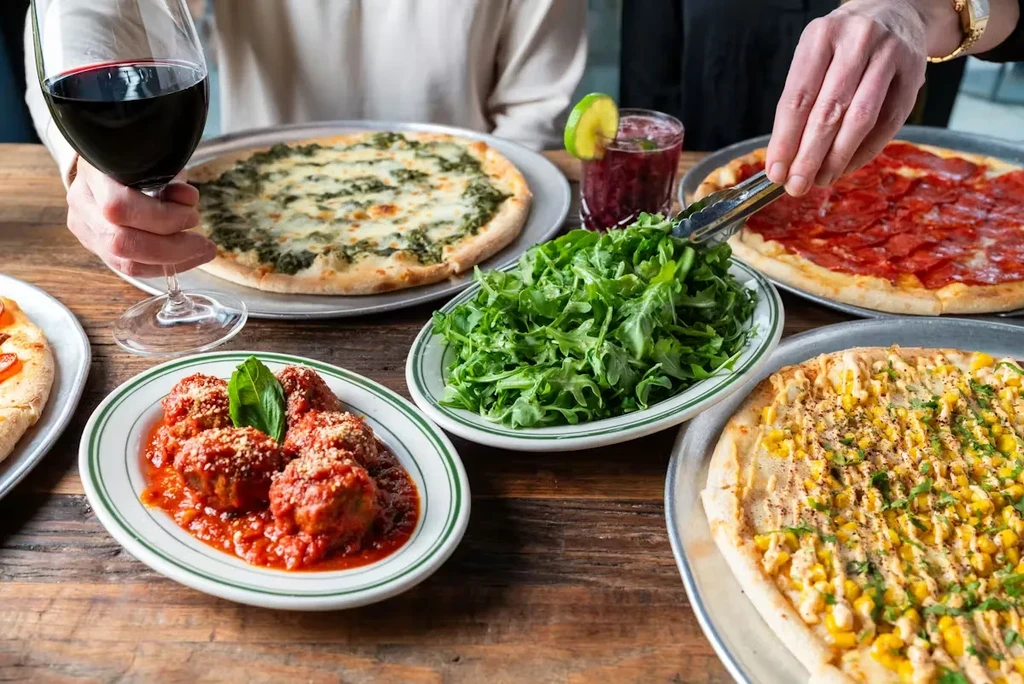 Restaurant table with pizzas, meatballs, arugula salad, and drinks.
