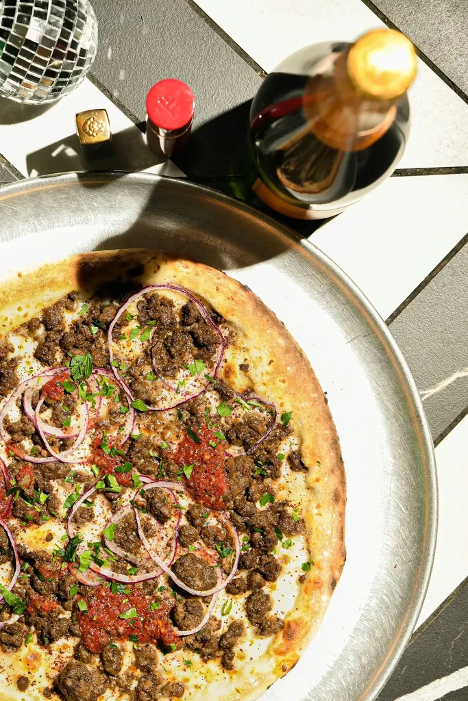 Close-up overhead of a cooked pizza with meat, sauce, onion, and herbs.