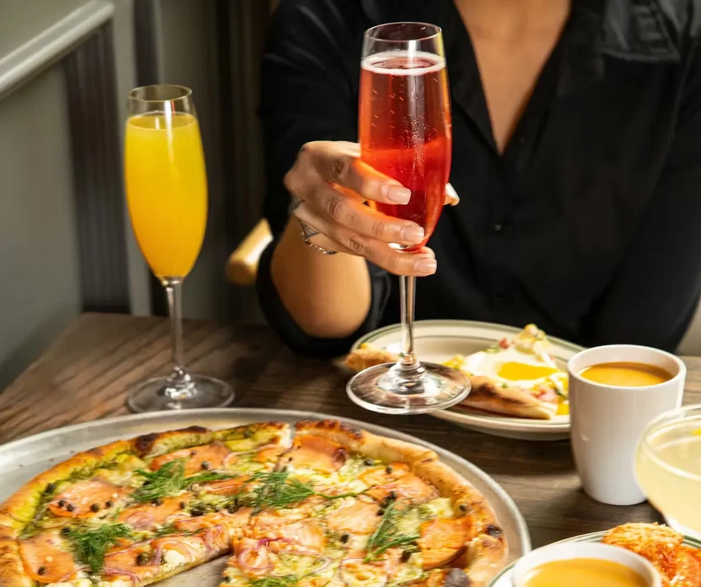 Smoked salmon pizza, fried eggs, and mimosas at a brunch table.