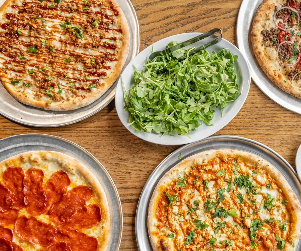 Four distinct pizzas and a green salad on a wooden table.