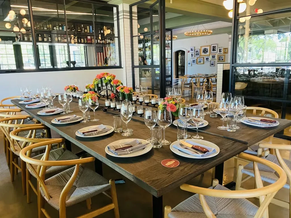 Long dining table in an upscale restaurant with flowers and formal settings.