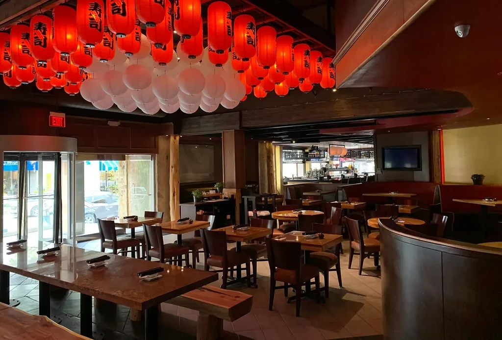 Restaurant interior with red Japanese lanterns, diverse seating, and warm lighting.