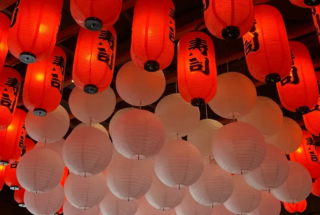 Ceiling filled with illuminated red sushi and white paper lanterns.