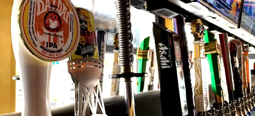 Close-up of diverse beer tap handles at a well-lit bar.