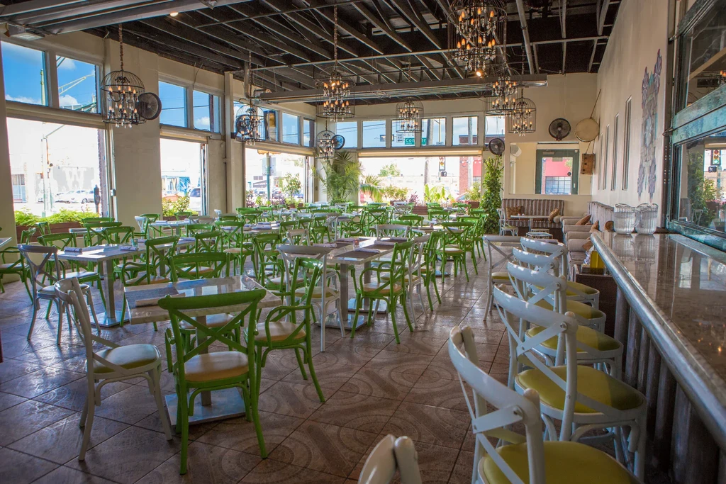 Spacious, empty restaurant with green chairs, industrial ceiling, and bar area.