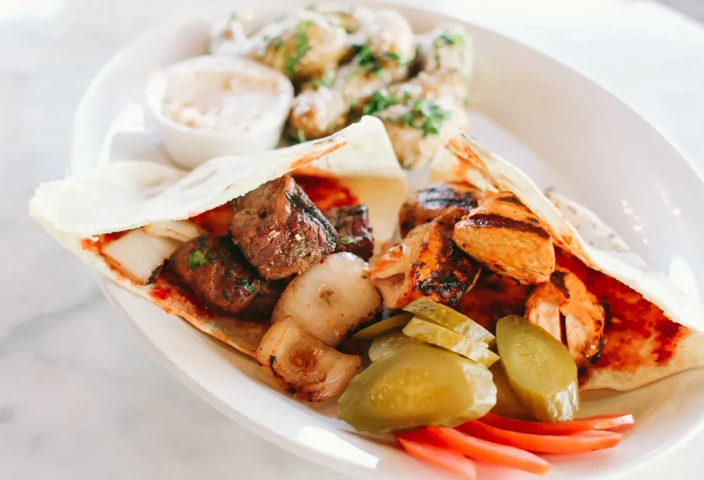 Grilled meat deconstructed wrap with onions, red sauce, pickles, and tomatoes.
