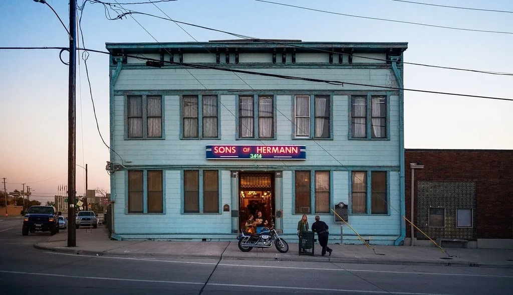 Teal Sons of Hermann building exterior at dusk with people and motorcycle.