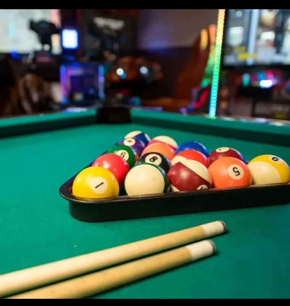 Colorful billiard balls racked on a green felt pool table with cues.