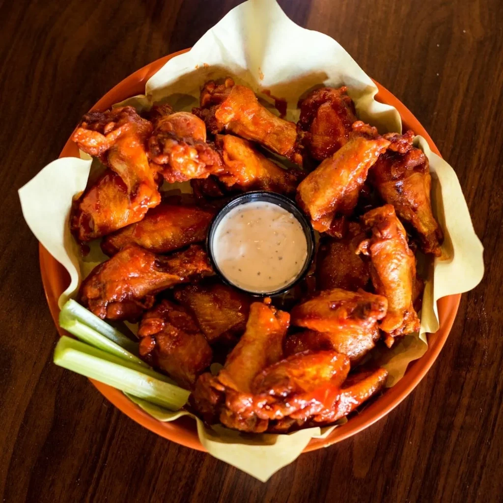 Bowl of sau saucy chicken wings, creamy dip, and fresh celery.