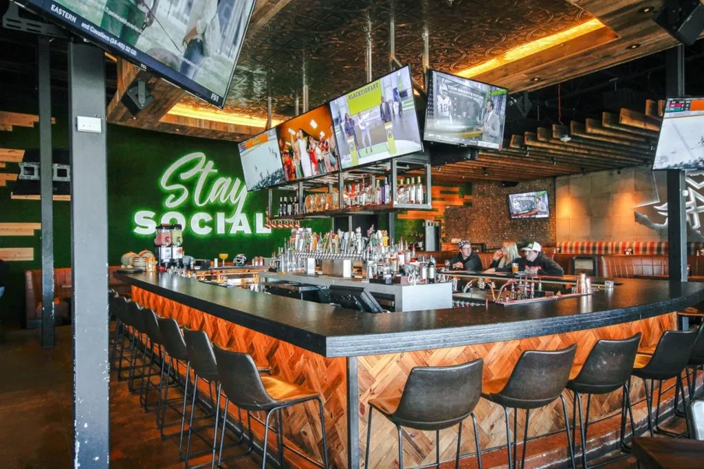 Modern bar interior with patrons, glowing counter, and 'Stay SOCIAL' neon.
