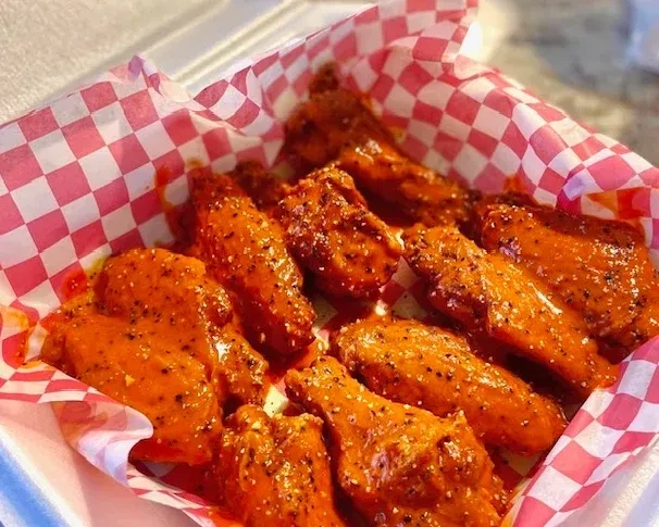 Hot wings with seasoning in a diner-style take-out container.